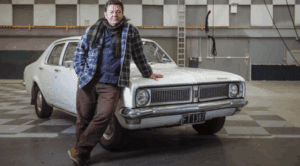 ドラマシェパード警部で使用されている1071年式の車、ホールデン・キングスウッドと、その車の前に立つシェパード警部役を演じる俳優ニール・ライ。